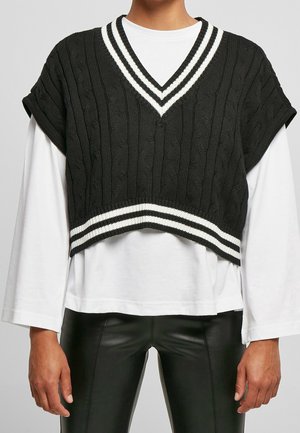 Black cable knit sleeveless V-neck vest with white stripes worn over a white long-sleeve shirt and black leather pants.
