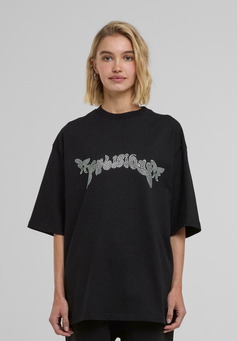T-shirt nera oversize in cotone, con una stampa lucida di strass che rappresenta un testo stilizzato sul petto. Maniche corte e scollatura rotonda.
