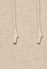 Beige hoodie-tyg med subtil textur, featuring flätade dragsko och rundade plastspetsar i matchande färg.