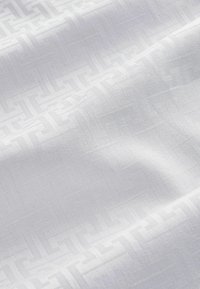 Weißer Stoff mit einem subtilen geometrischen Muster, der eine strukturierte Oberfläche und ein weiches, glattes Erscheinungsbild aufweist.