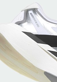 Κοντινή λήψη της φτέρνας του λευκού και ασημί αθλητικού παπουτσιού Adidas Adizero Evo SL EXO με μαύρες λεπτομέρειες στη μεσαία σόλα και διαφανή εξωτερική σόλα.