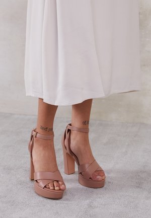 Sandalias de tacón alto en color nude con plataforma, que cuentan con tiras cruzadas sobre los dedos y una correa en el tobillo, hechas de material suave.