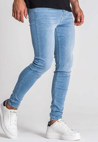 Jean skinny bleu clair en denim avec une texture lisse. Dispose d'un design classique à cinq poches et d'une fermeture à glissière. Accompagné de baskets blanches.