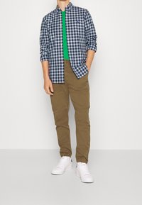 Kostkovaná modro-bílá košile, pod ní zelené tričko, béžové kalhoty a bílé tenisky. Neformální oblečení s košilí na knoflíky a kapsami.