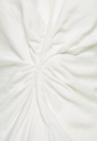 Vitt tyg med rynkad sömdetalj som skapar en tvinnad, volangliknande textur i mitten.