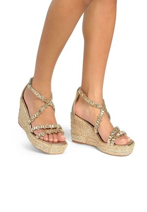 Sandalias de cuña con suela de yute trenzado natural, acentos en tono dorado, correas entrecruzadas y un detalle de cuentas en la parte frontal.