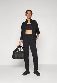 Crna jakna na patentni zatvarač, crni kratki top i crne hlače uskog kroja. Dodaci uključuju tamno zelenu torbu s crnim detaljima i crne tenisice.