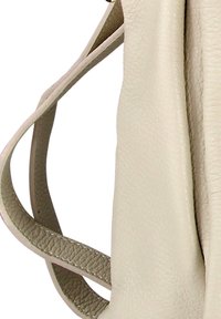 Close-up van de textuur van een beige leren tasriem en een glad leren zijkantpaneel met stikseldetails.