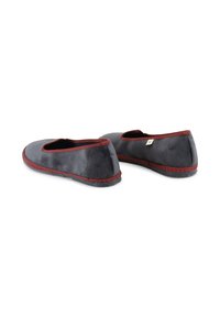 Zapatos de tela negros tipo slip-on con perfil bajo, ribete rojo y suela texturizada. Material suave con un diseño simple y redondeado.