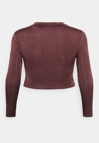 Top cropped de manga longa na cor bordeaux, feito de um tecido brilhante e suave. Apresenta um decote discreto e uma silhueta ajustada com detalhes mínimos.