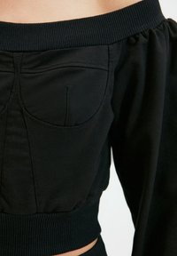 Schwarzes Cropped Top mit schulterfreiem Ausschnitt, geripptem Saum und seitlichen Taschen, aus einem glatten, dehnbaren Stoff gefertigt.