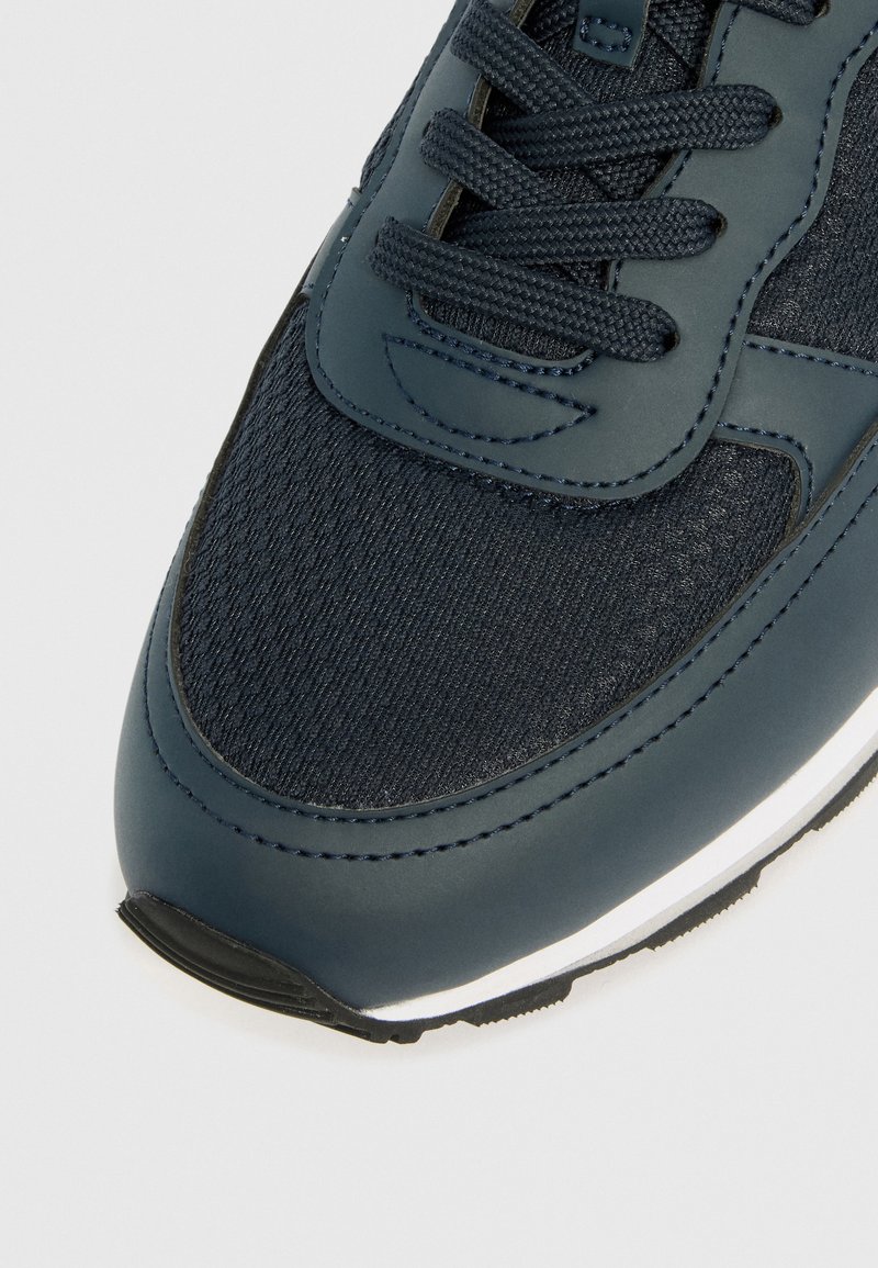 Baskets navy avec une tige en tissu texturé et des accents en cuir lisse, des lacets plats et une semelle en caoutchouc blanche. Design à bout arrondi.