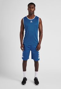 Blauwe sporttanktop met witte accenten, gecombineerd met blauwe shorts met witte chevronstrepen. De stof lijkt licht en ademend te zijn.