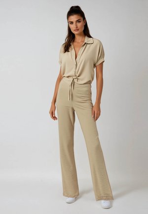 Beige blouse met opgerolde mouwen en een geknoopte strik in de taille, gecombineerd met bijpassende flared broeken. Glad, lichtgewicht materiaal.