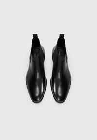 Botines negros de cuero con un diseño elegante, punta afilada, paneles laterales elásticos y tiradores para facilitar su uso. Textura suave, con un minimalismo en los detalles.
