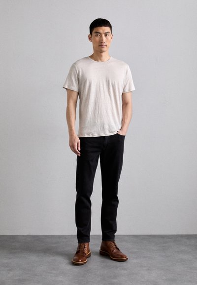 Camiseta de manga corta gris claro combinada con jeans negros ajustados y zapatos de cuero marrón con cordones sobre un fondo liso.