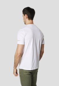 T-shirt blanc à manches courtes en coton, avec un col rond et un logo imprimé en jaune sur la manche gauche.