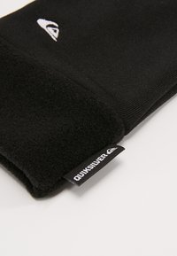 Čierna flísová rukavica so hladkým materiálom a textúrovaným manžetom, s bielym logom a čiernou etiketou s nápisom "Quiksilver" v bielom písmene.