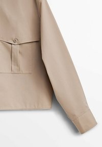 Chemise beige à manches longues avec fermeture à boutons, dotée d'une poche plaquée et d'un tissu en coton lisse. Design simple avec un ourlet droit.