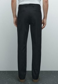 Černé kalhoty rovného střihu, s zadními kapsami a poutky na opasek, kombinované s hnědými botami. Hladká látka s jednolitou strukturou.