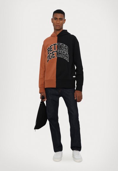 Hooded sweatshirt featuring a split design in black and brown with "BETTER 2GETHER" printed in white. Paired with dark jeans and white sneakers.