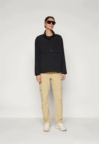 Juodas megztinis su puse užtrauktuko ir priekinė kišenė, derinamas su smėlio spalvos krovinių kelnėmis ir baltais batais, pasižymintis lygiu paviršiumi.