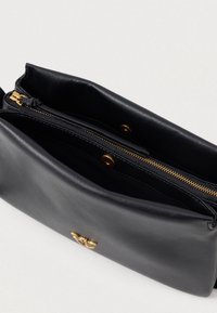 Černá kožená taška s hladkým povrchem, vybavená zlatým zipem a zacvakávacím uzávěrem. Uvnitř má přihrádku pro organizaci.