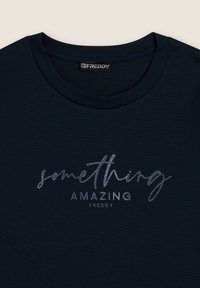 T-shirt blu navy con scollo tondo. Presenta una scritta in metallo argento che dice "qualcosa di INCREDIBILE" e "FREDDY" sotto. Texture morbida.