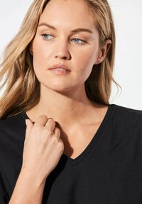 Schwarzes V-Ausschnitt-T-Shirt aus leichtem Stoff, mit lockerem Schnitt und kurzen Ärmeln. Der Hautton ist an der Schulter und der Hand sichtbar.