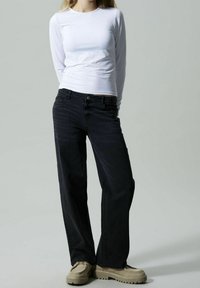 Biała bluzka z długim rękawem połączona z ciemnoniebieskimi dżinsami o prostym kroju. Dżinsy mają klasyczny styl pięciu kieszeni i delikatne przetarcia. Obuwie: beżowe buty na platformie.