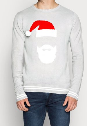 Mand iført lysegrå sweater med motiv af hvid julemands skæg og rød julehue, kombineret med blå jeans.