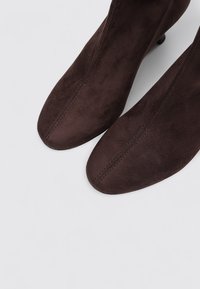 Bottes de cheville en daim brun foncé avec un design à bout pointu, présentant une texture lisse et des détails de couture minimalistes.