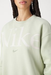 Light green crewneck sweatshirt with large white "Nike" text and small green swoosh logo. Soft fabric, relaxed fit, and simple design.