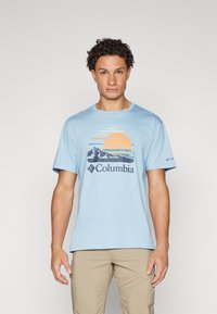 Lyseblå bomulls t-skjorte med grafisk design av en sol og fjell i oransje og marineblått, med "Columbia" merke under.