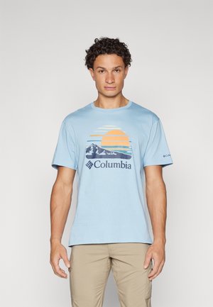T-shirt en coton bleu clair avec un design graphique représentant un soleil et des montagnes en orange et marine, avec la marque "Columbia" en dessous.