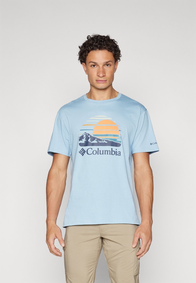 Lyseblå bomulls t-skjorte med grafisk design av en sol og fjell i oransje og marineblått, med "Columbia" merke under.