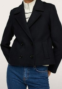 Cappotto doppiopetto blu navy realizzato in tessuto testurizzato, con grandi bottoni neri, ampie rever e un design accorciato.