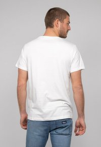 T-shirt en coton blanc à manches courtes, col rond et coupe droite. Porté avec un jean denim bleu clair. Design simple et sans ornement.
