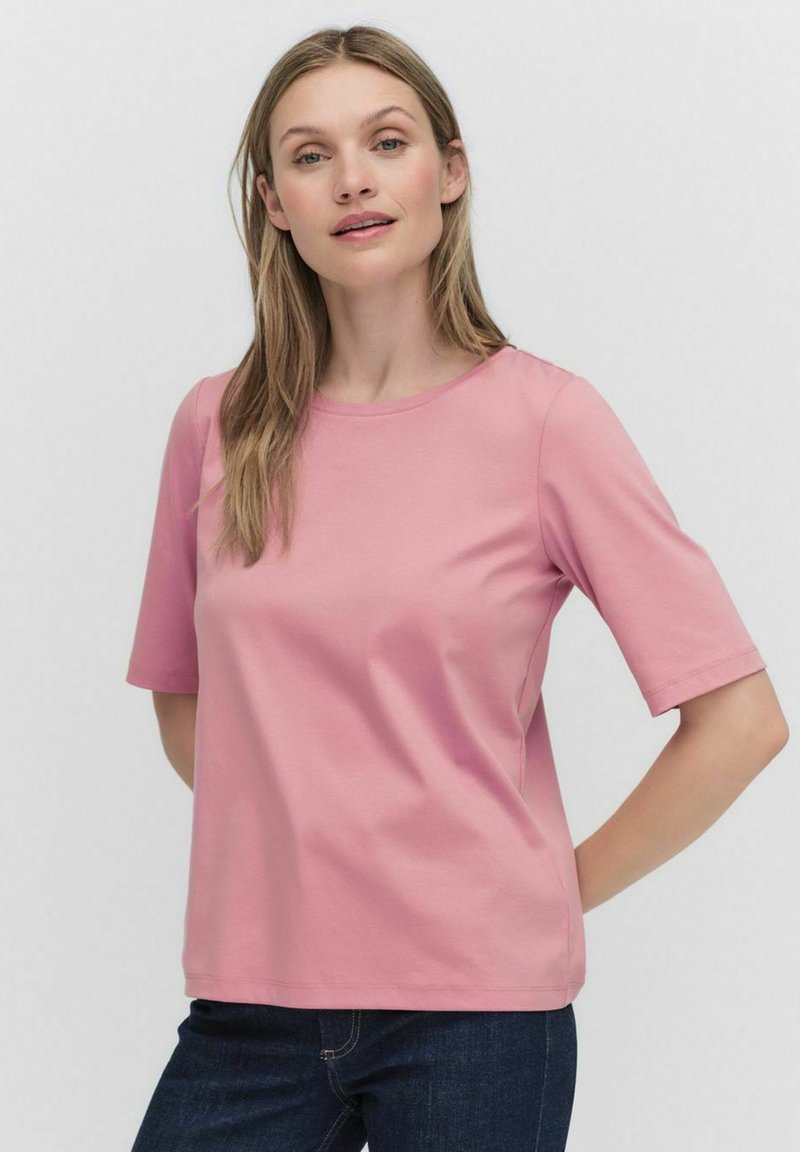 Kortärmad rosa bomullsskjorta med rund halsringning, slät textur och avslappnad passform, i kombination med mörkblå jeans.