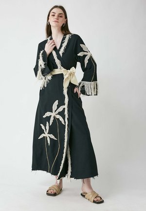 Black long dress with white floral embroidery, fringed sleeves, and a beige tie belt. The fabric has a textured finish.
