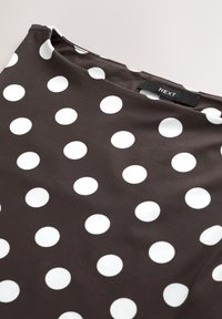 Tissu noir avec de grands pois blancs, avec une étiquette de marque "NEXT" cousue près de l'encolure.