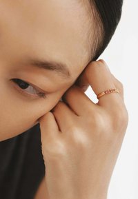 Anillo de oro con una fila de pequeñas piedras preciosas rosa y claras, usado en un dedo. La piel es de tono claro y tiene una textura suave.