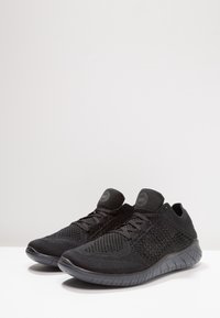 Zapatillas deportivas negras con una parte superior de malla, punta redondeada y suave, y una suela texturizada con un diseño flexible para mayor comodidad y soporte.