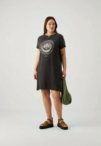 Melnas kokvilnas T-kreklu kleita ar lotosa grafiku, apaļu izgriezumu, īsām piedurknēm un A formas siluetu. Kombinēta ar brūnām sandālēm un zaļu somiņu.