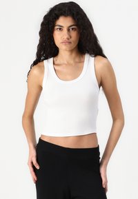 White ribbed tank top with a scoop neckline and a cropped fit, paired with high-waisted black pants; smooth texture and sleeveless design.