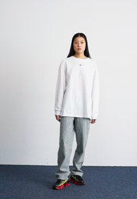 Fehér, hosszú ujjú Nike póló, szürke csíkos nadrág és fekete tornacipő piros részletekkel. Egyszerű dizájn, könnyű anyag és laza fazon.