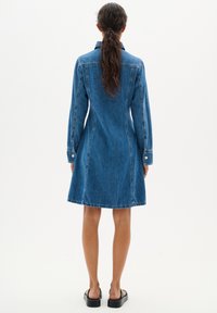 Robe chemise en denim avec un buste ajusté, une jupe évasée, des manches longues, un col classique et des boutons en argent sur les poignets, dans un bleu moyen.
