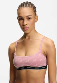 Roze bralette met wit "Hugo" patroon, verstelbare bandjes en een zwarte elastische band met de merknaam. Zachte stof, aansluitend ontwerp.