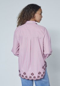 Lyserød og hvid stribet skjorte med rund kant, prydet med mørk blomsterbroderi langs bunden og en rygsøm-design.