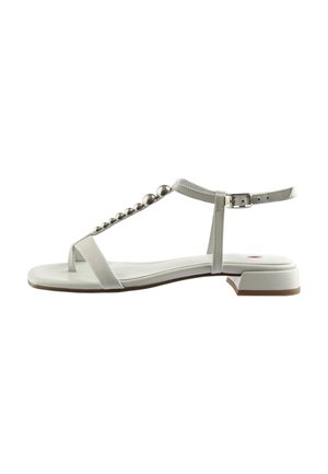 Sandales blanches en cuir avec un design à T, une pointe arrondie et des billes métalliques le long de la lanière. Talon plat et fermeture à boucle à la cheville.